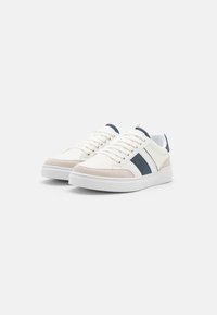 Weiße Sneakers mit marineblauen und beige Akzenten, ausgestattet mit einem glatten Leder-Obermaterial, strukturierten Wildleder-Overlays und flachen Schnürsenkeln auf einer Gummisohle.