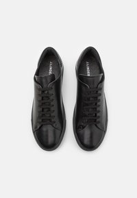 Ett par svarta lädersneakers med snörning, rundad tå och texturerade innersulor, märkt "J.Lindeberg", på en vit bakgrund.