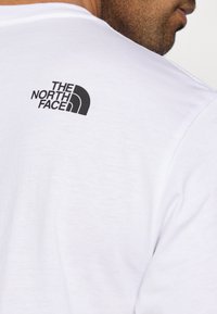 Λευκό βαμβακερό t-shirt με μαύρο λογότυπο "THE NORTH FACE" πάνω στην πίσω πλευρά. Ομαλή υφή με κανονική λαιμόκοψη.