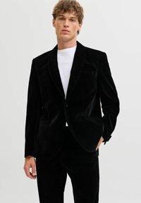 Melna samta žakete ar šaula apkakli, diviem priekšējiem kabatām un vienas pogas aizdari. Valkāta virs baltās krekliņas, kas ir ar maigu spīdumu.