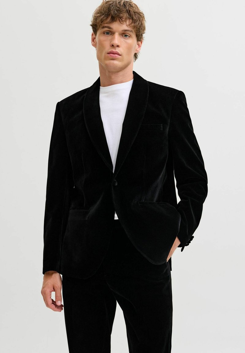 Melna samta žakete ar šaula apkakli, diviem priekšējiem kabatām un vienas pogas aizdari. Valkāta virs baltās krekliņas, kas ir ar maigu spīdumu.