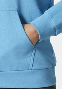 Jasnoniebieska bluza z kapturem z przednią kieszenią i ściągaczami. Miękka tekstura z przeszyciami wokół kieszeni i dołu.