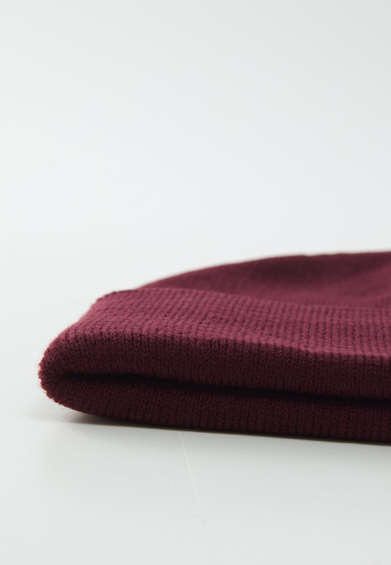 Bordeaux gebreide beanie, keurig gevouwen, met een gemêleerd patroon en zachte, rekbare stof. Eenvoudig ontwerp zonder extra accenten of bevestigingsmaterialen.