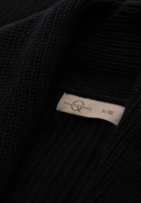 Czarny wełniany kardigan z teksturowanym wzorem, z widoczną metką z napisem "Quintessence" oraz rozmiarem "M/48."