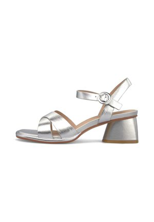 Sandalia plateada con puntera abierta, correas frontales cruzadas, correa con hebilla en el tobillo y tacón bajo en bloque sobre fondo blanco.