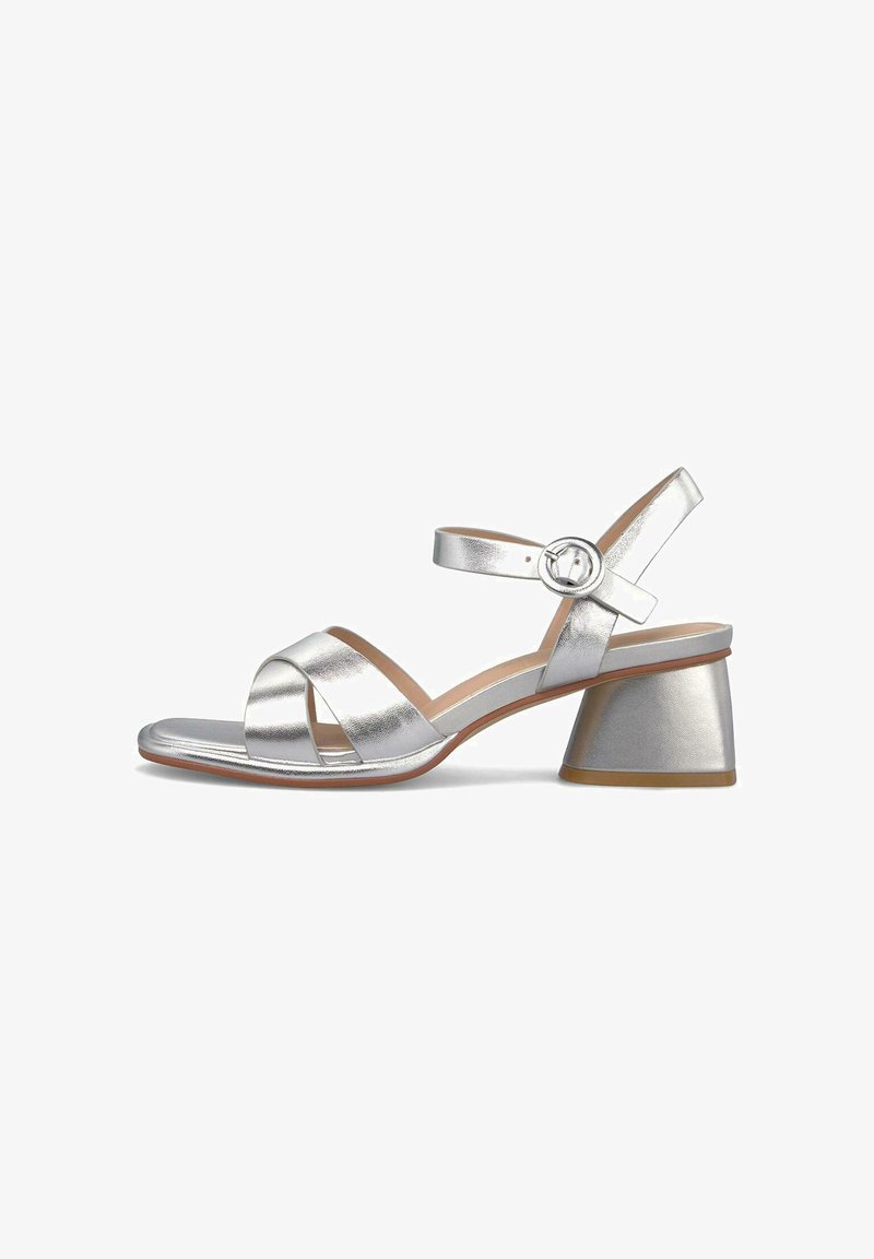 Sandale argentée à bout ouvert avec des brides croisées à l'avant, une bride réglable à la cheville et un petit talon carré sur fond blanc.