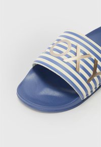 Blå og hvit stripete slide sandal med en bred stropp som har bronsebokstaver, teksturert fotseng og flat gummisåle.