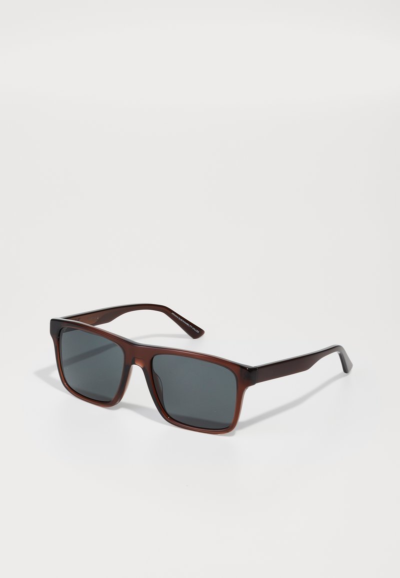 Ochelari de soare din plastic maro, cu lentile gri închise, formă rectangulară, textură netedă și accente negre contrastante pe brațe.