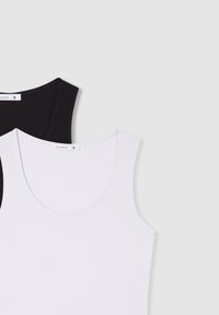 Top in cotone bianco e nero senza maniche con scollo rotondo. Il top nero è indossato sopra quello bianco, mettendo in mostra trame morbide e design semplici.