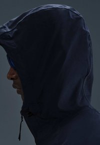 Mörkblå huva jacka med hög krage och strukturtyg; har en dragkedja och en justerbar dragsko vid halsen.