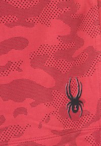 Tejido rojo con un patrón de camuflaje texturizado y con puntos. Presenta un logo de araña negra en la esquina inferior derecha. Material suave y atlético.
