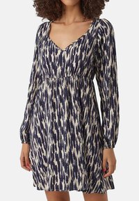 Robe à motifs bleu marine et crème avec des manches longues, un col en V et une taille froncée. Le tissu a une apparence texturée et tissée.