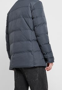 Chaqueta acolchada gris oscuro con detalles de costuras diagonales y un corte cómodo. Cuenta con un cuello alto y puños ajustables para mayor calidez.