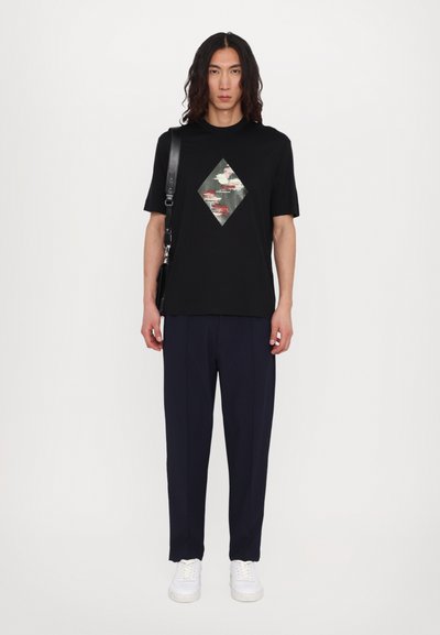 Tricou negru cu un design grafic multicolor în formă de diamant, asortat cu pantaloni bleumarin și adidași albi. Linii simple și curate.