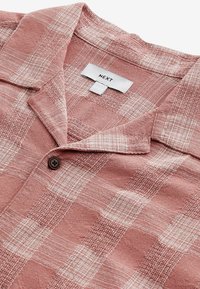 Camisa de manga corta con cuello en color rosa empolvado, con un patrón de cuadros, tejido texturizado, un botón marrón y una etiqueta que dice "NEXT."
