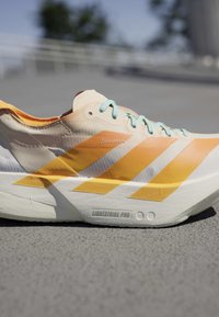 Lichtgewicht oranje-witte hardloopschoen met lichtblauwe veters op een verharde ondergrond, met "Lightstrike Pro" dempingstechnologie.