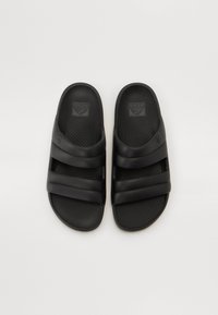 Sandales en caoutchouc noir avec deux larges brides et semelle texturée ; présente le logo sur la semelle intérieure et une semelle plate pour un enfilage facile.