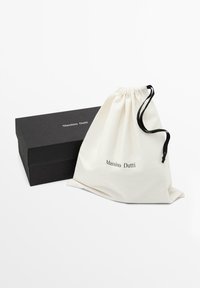 Bavlněná taška na stažení v krémové barvě s nápisem "Massimo Dutti" černě, vedle matně černé obdélníkové krabičky.