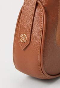 Brun læderhandtaske med tekstur i en afrundet form, der har en syet kant og et gyldent logo som accent på siden.