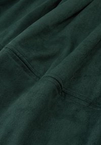 Tissu en daim vert avec une texture douce, présentant des coutures plates et de subtiles réflexions lumineuses. Le matériau semble lisse et légèrement pelucheux.