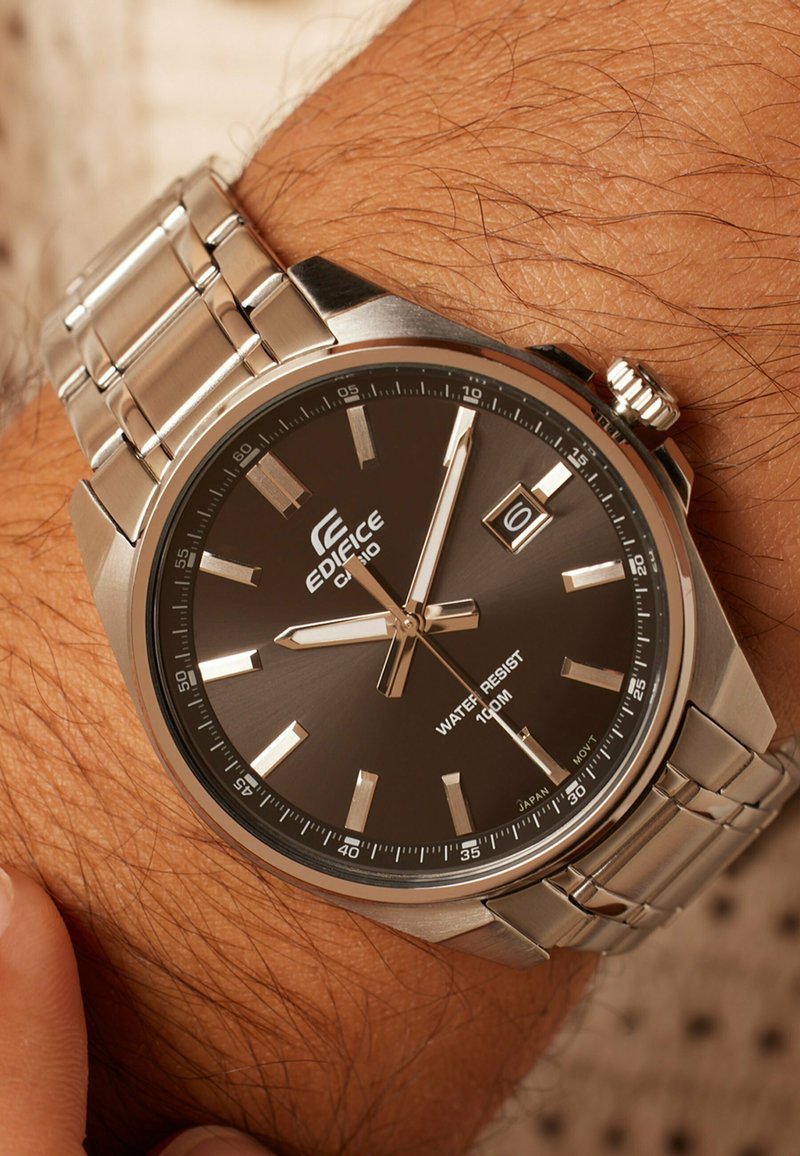 Silver wristwatch with a dark brown face, stainless steel bracelet, and luminous hour markers. Features a date display and water resistance up to 100m.