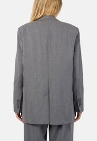 Blazer grigio realizzato in tessuto testurizzato, caratterizzato da una vestibilità su misura, revers a punta e quattro bottoni sui polsini. Dettaglio visibile della cucitura posteriore.