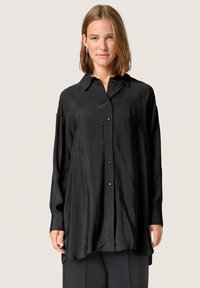 Camisa negra de manga larga en una tela suave y brillante con botones en la parte delantera y un cuello clásico. Presenta un ajuste ligeramente oversized.