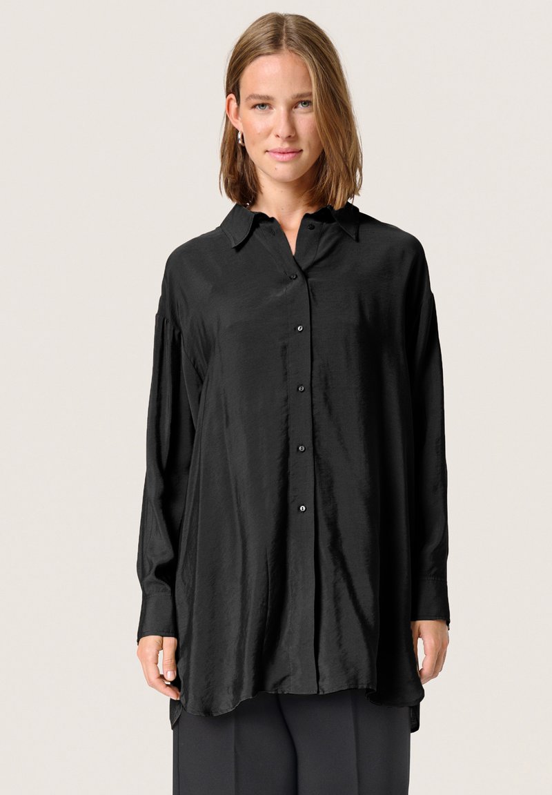Camisa negra de manga larga en una tela suave y brillante con botones en la parte delantera y un cuello clásico. Presenta un ajuste ligeramente oversized.