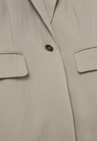 Lichtbeige blazer van textuurstof, met een enkele knoopsluiting en twee voorzakken met klepdetails.