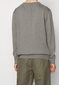 Grijze crewneck trui gemaakt van zachte, gestructureerde stof, met ribbelboorden en onderrand. Gecombineerd met losvallende olijfgroene broek.