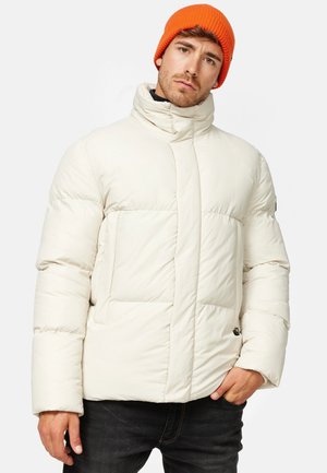 Doudoune off-white, avec un col haut, des coutures horizontales et des poches latérales. Associée à un bonnet en tricot orange vif.
