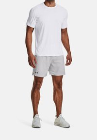 Vit kortärmad träningströja med rund halsringning, tillsammans med ljusgrå shorts med en logo, och vita skor med en texturerad yta.