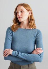 Top cu mâneci lungi, tricotat cu model în dungi, de un albastru delicat, având o croială cu gât rotund. Modelul are brațele încrucișate, evidențiind designul ajustat și textura.
