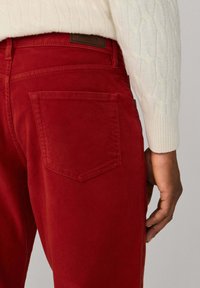 Pantalones de pana rojos con una textura distintiva, con un bolsillo trasero único, combinados con un suéter de punto trenzado crema.