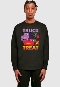 Melnas garās piedurknes T-krekls ar krāsainiem multfilmu automobiļiem un tekstu "TRUCK OR TREAT" biezajās burtiem; ikdienišķs piegriezums un kokvilnas materiāls.