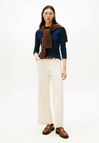 Navy blaues Langarmoberteil, cremefarbene weite Hose, brauner gestrickter Schal und braune Mokassins mit dicker Sohle. Schlichte, lässige Outfits an einem Model.