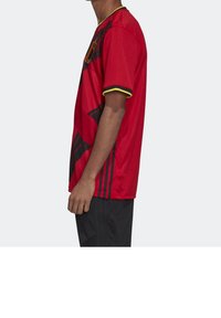 Maglietta sportiva rossa con maniche corte, caratterizzata da strisce diagonali nere e dettagli gialli al colletto e ai bordi delle maniche. Tessuto leggero.