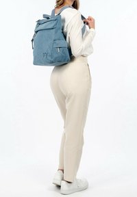 Blå denimryggsäck med ett lock, dragkedjestängning och framficka. Har justerbara remmar och en mjuk textur. Förstärkt sömnad synlig.