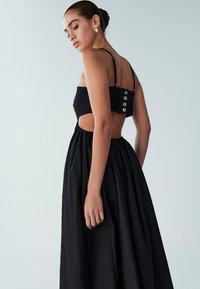 Must kleit, millel on liibuv korsett ja avatud selg. Omadused hõlmavad õhukesi rihmu, dekoratiivseid nuppe ja mahukat, kogutud seelikut. Pehme tekstuur.