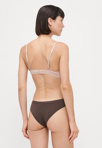 Smeđi bikini set koji se sastoji od svijetloružičastog grudnjaka s tankim trakama i kopčanjem, u kombinaciji sa čvrstim smeškim donjim dijelom sa visokim strukom.