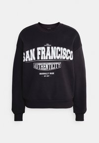 Sudadera negra de tejido suave, con texto blanco en negrita: "AUTENTICIDAD DE SAN FRANCISCO" y "HECHO ORIGINALMENTE EST. 1997." Puños acanalados.