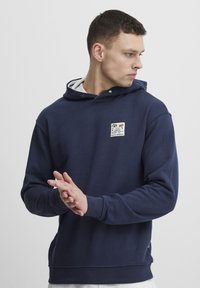 Blue cotton hoodie with a front pocket, drawstring hood, and a graphic patch featuring palm trees. Ribbed cuffs and hem.