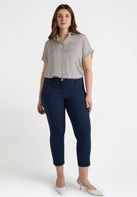 Kevyt, lyhythihainen paita, jossa on geometrinen kuvio valkoisena, laivastonsinisenä ja keltaisena, yhdistettynä laivastonsinisiin istuviin housuihin ja vaaleisiin korkokenkiin.