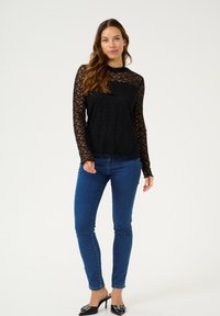 Un haut en dentelle noire à manches longues avec un décolleté et un ourlet festonnés. Associé à un jean bleu ajusté et des mules à talons noirs, mettant en avant un design texturé.