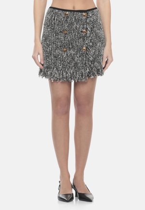 Donna che indossa una minigonna in tweed bianco e nero con bottoni dorati e orlo con frange, abbinata a tacchi slingback neri.