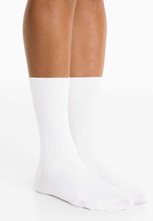 Witte katoenen crewsokken met ribbeltextuur, die tot halverwege de kuit reiken. Voorzien van een ronde teen en een verstevigde hak voor duurzaamheid.