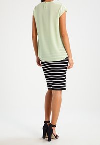 Ljusgrön blus med kort ärm och bakknäppning, parat med en svartvit randig pennkjol och svarta klackskor med ankelsnöre.