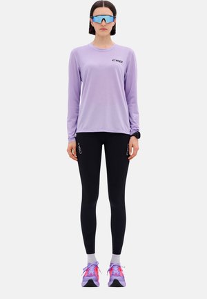 Light purple long-sleeve top with black logo, paired with black leggings, and colorful sneakers featuring pink and purple accents.