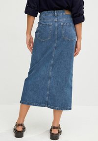 Denim nederdel i mellemblå, midt på læggen længde med en klassisk pasform. Har lappet lommer og en simpel kant med diskrete syninger.