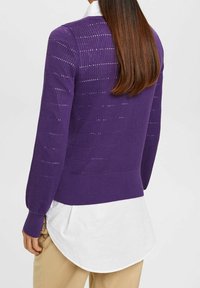 Pull violet en maille avec un motif texturé, bords-côtes aux poignets et à l'ourlet, porté sur une chemise blanche, avec une coupe décontractée.